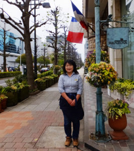HANZOYAグループの屋外緑化を担当する嶋崎有紀恵さん。メンバー4人の中心となって活躍している。フランス料理HANZOYAは横浜アリーナ（左）に面した場所に立地している