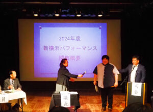 商工部長の鳥谷尚道さん（最右）から田原さんがバトンを託され「新横浜パフォーマンス」についての説明をスタート
