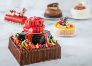 「ガトー・シュルプリーズ・オ・ショコラ」（手前）は“ショコラの贈り物”として、近年なかったサイズ感・価格での提供。大きなショコラのリボンをあしらい、「華やかで豪華な」クリスマスケーキに仕上げている（同ホテル提供）