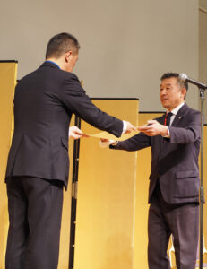 竹下区長から表彰状を受け取る金澤さんは一般社団法人F・マリノススポーツクラブの代表理事に2024年4月から着任した