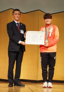 中田さんは2年ほど前から港北区在住。竹下区長から表彰状を受け取り笑顔に